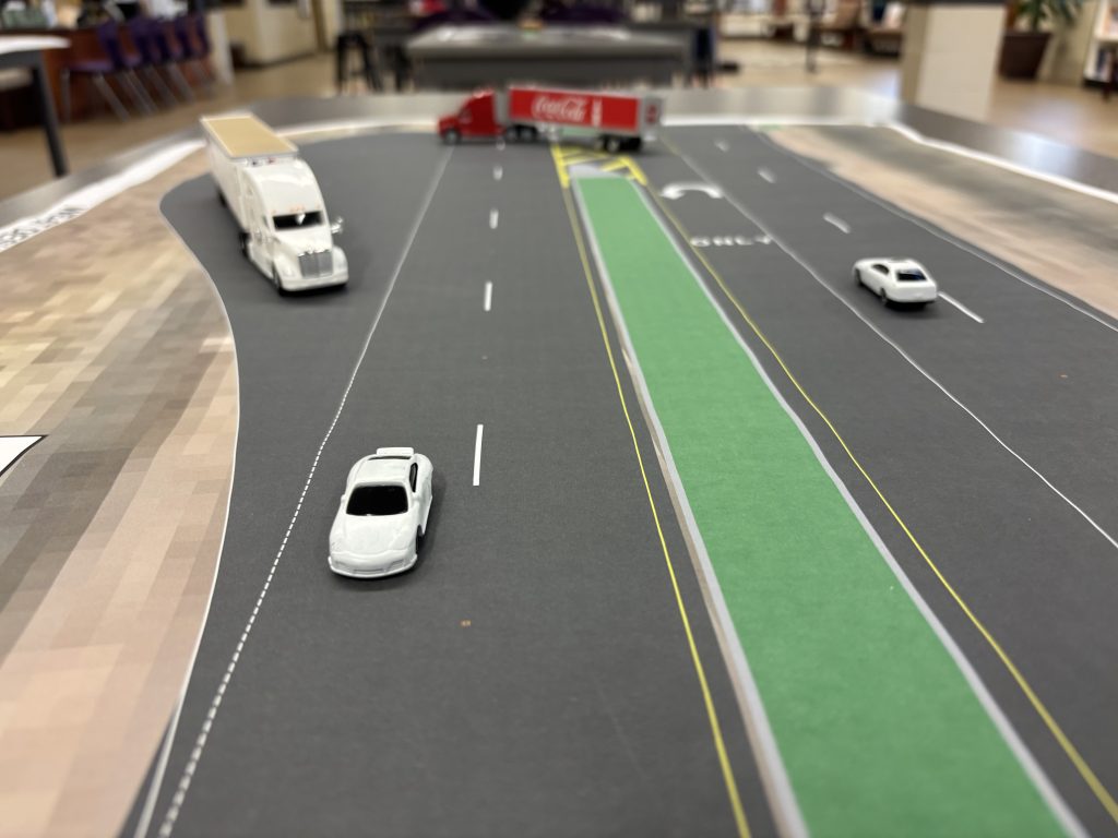 Model vehicles on a scale map demonstrate how loons — large, paved areas in the shoulder of the highway — help larger vehicles with complete U-turns.