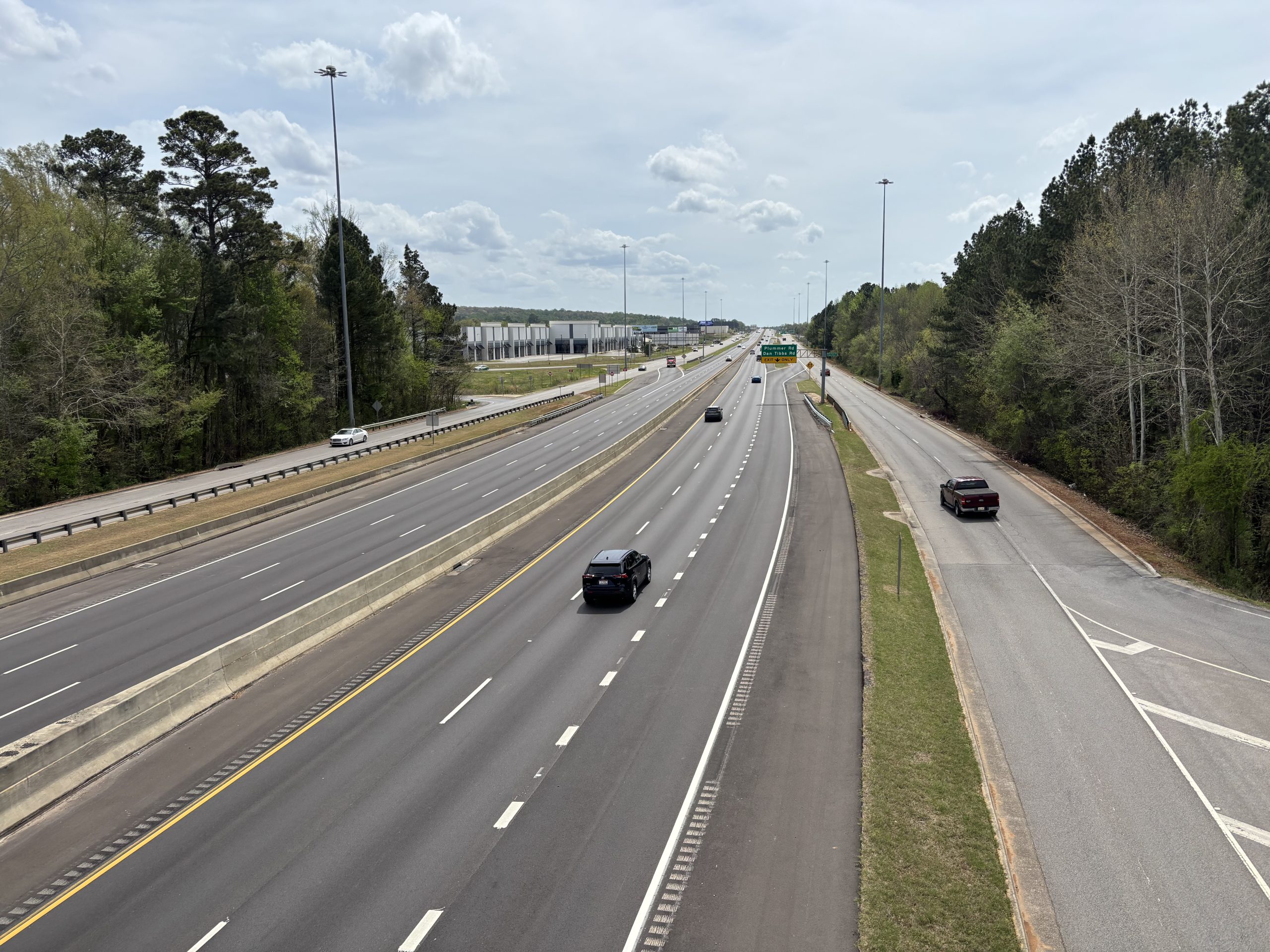 Traffic travels on a divided highway with limited access and service roads on either side. Last year's resurfacing of the mainline is apparent from the darker color of the pavement.