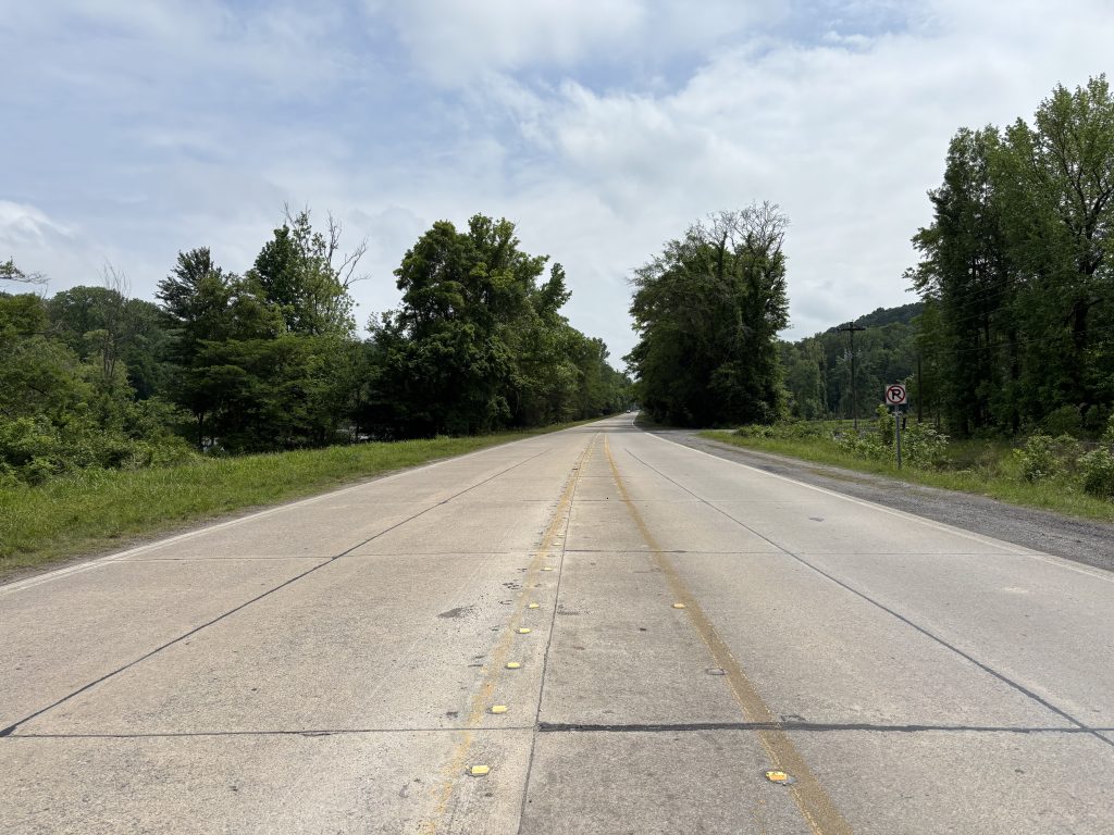 A divided four-lane highway narrows to two lanes. The  joints of the concrete slabs that form the road are visible.