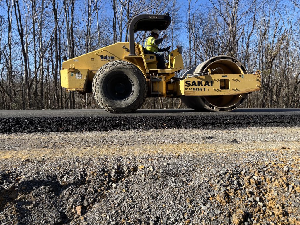 A roller rolls over a road in profile, showing the build-up of the roadway.