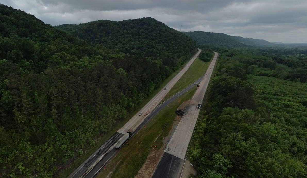 An four-lane interstate going through mountains with a grassy median between the roadways. A single-lane temporary road crosses the median from one roadway to the other.