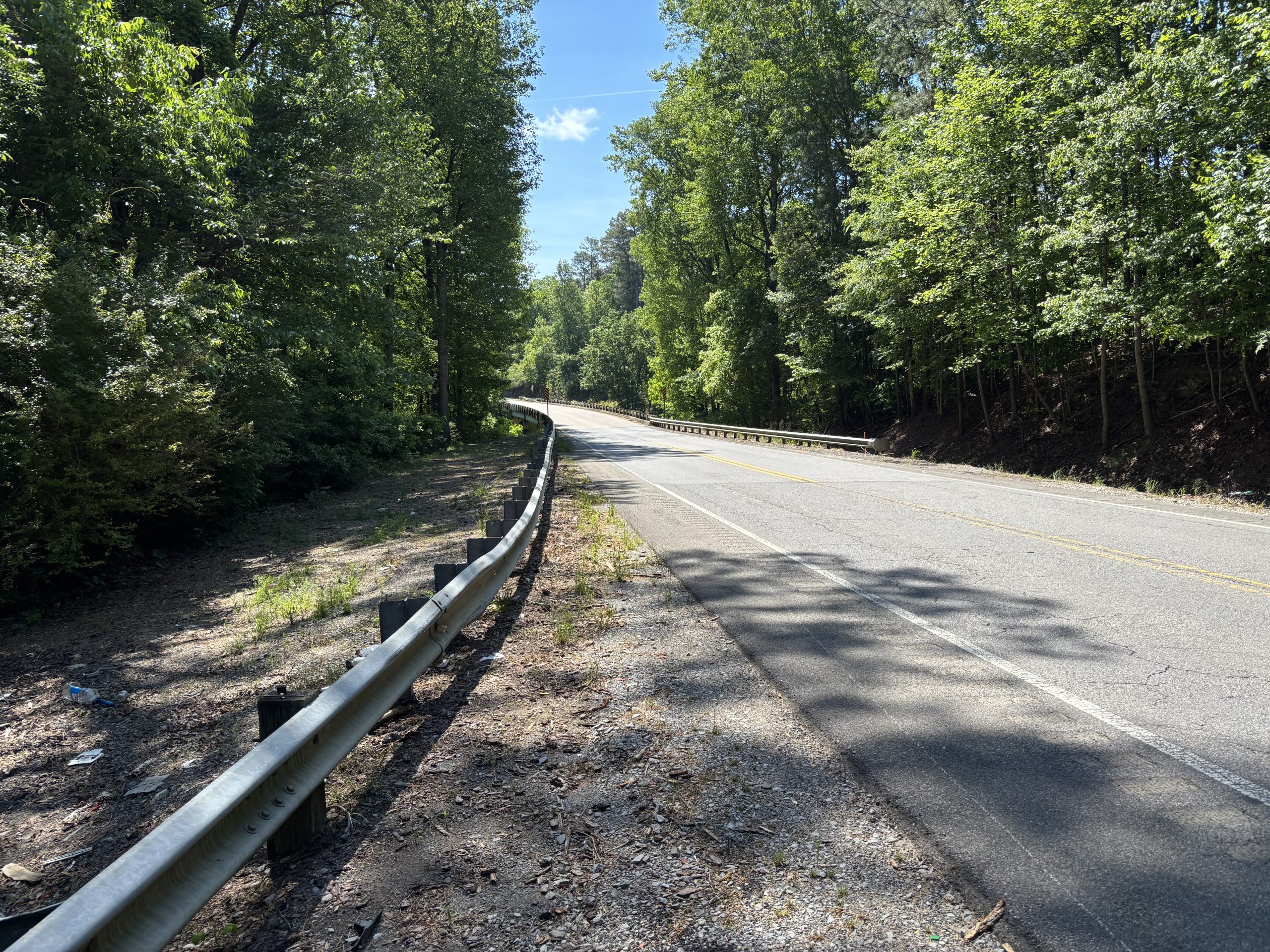 A two-lane highway crossing a bridge in a wooded area.