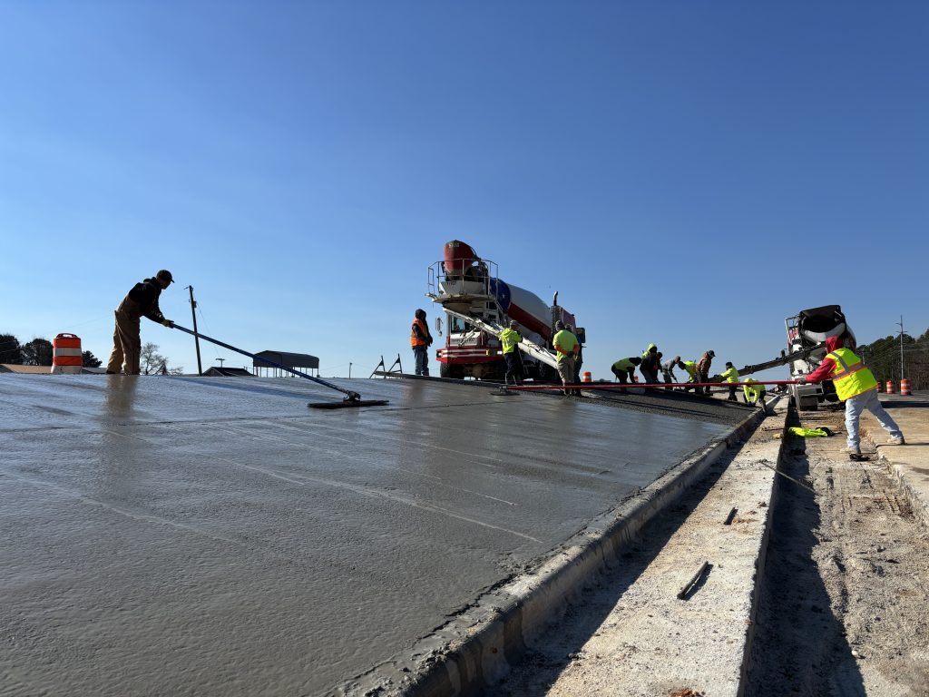 Workers use tools to finish finish freshly-poured concrete in a highway median.