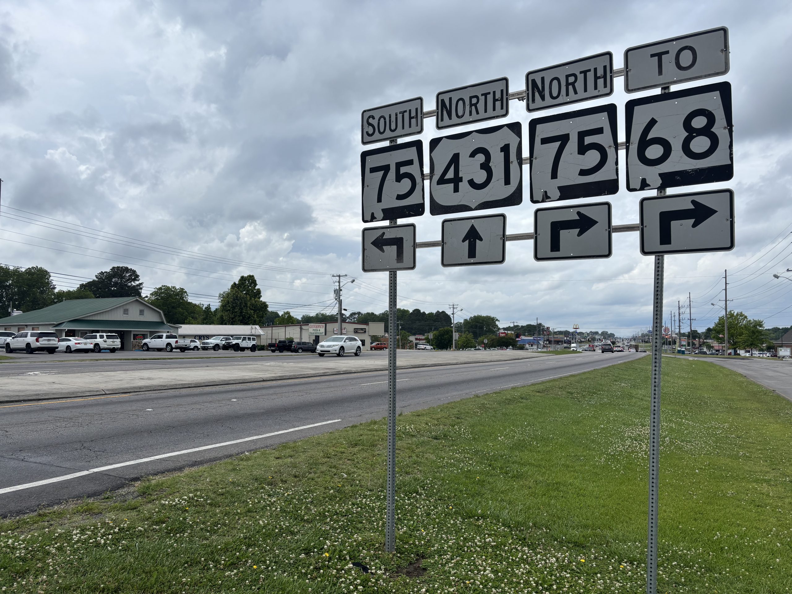 A cluster of signs for US-431 and SR-75 mark a divided four lane highway. In the background, traffic queues at a busy intersection.
