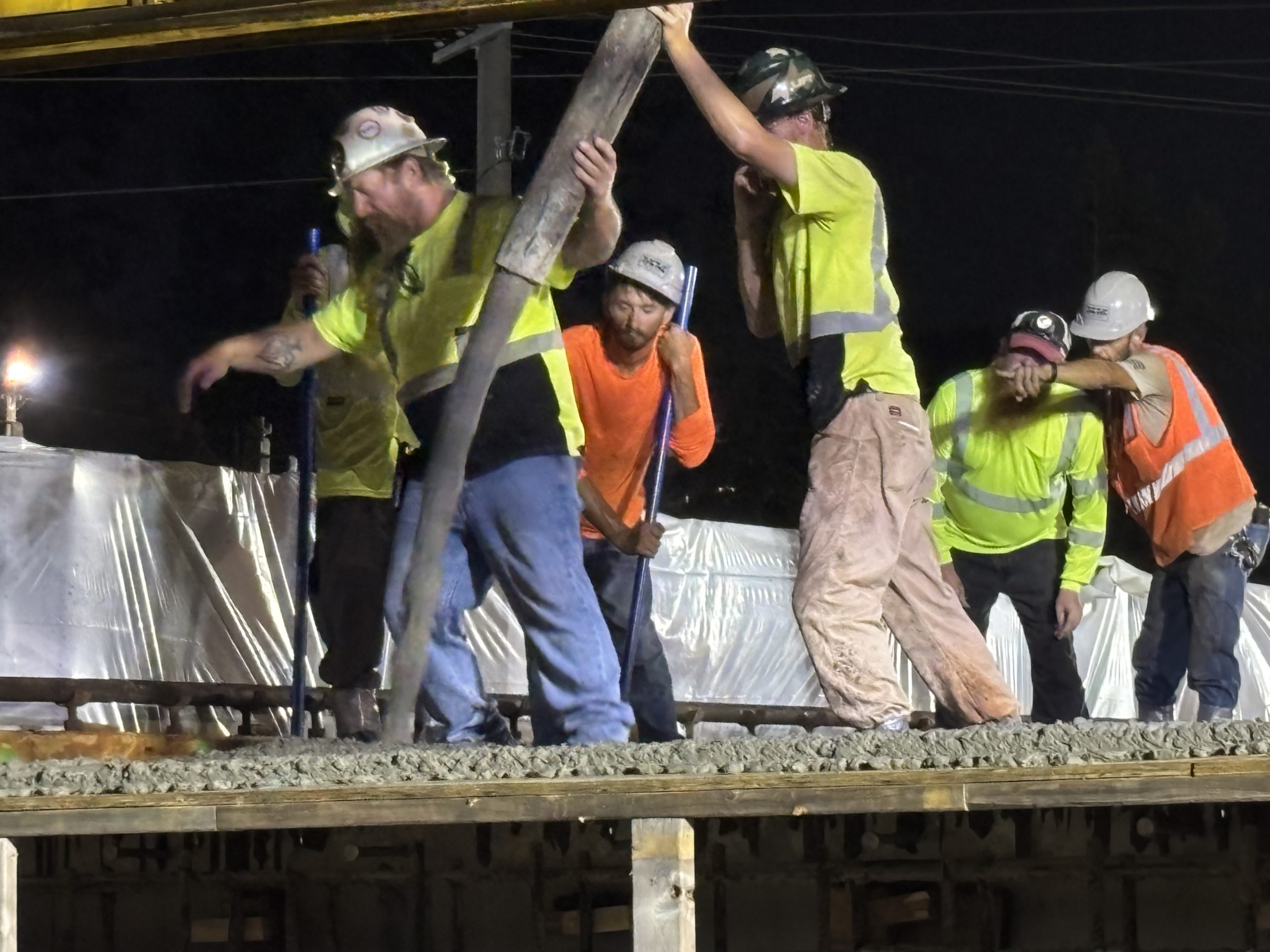 Workers direct a boom pouring concrete on a bridge