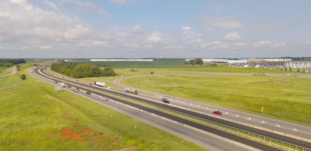 An interstate highway that is being expanded to six lanes, On each side, the newly-paved inside lanes are separated from the outer two lanes by concrete barriers.