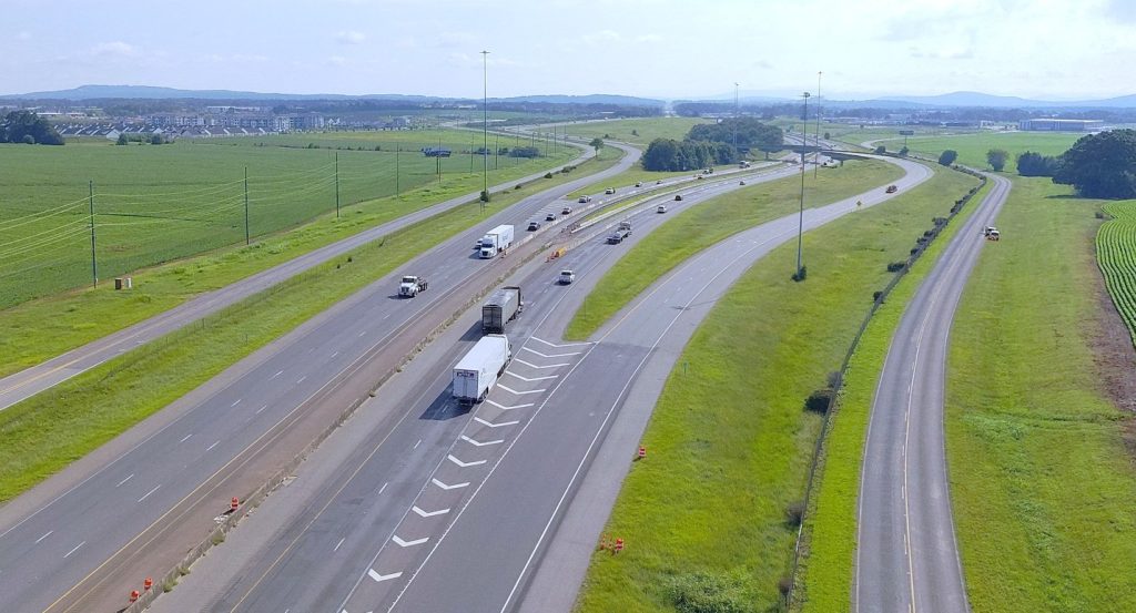 An interstate highway that is being expanded to six lanes, On each side, the newly-paved inside lanes are separated from the outer two lanes by concrete barriers.