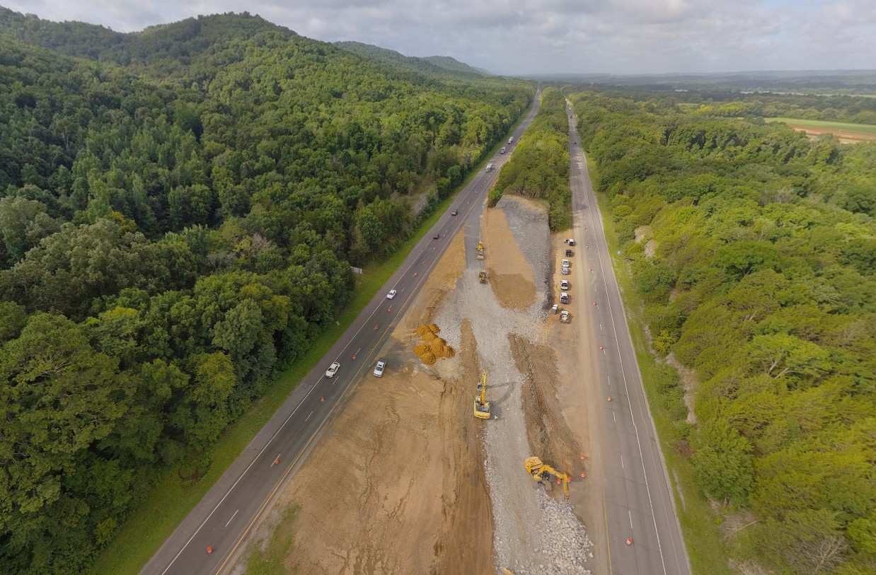 An erial view of a crossover being constructed across a rocky median between two interstate roadways.