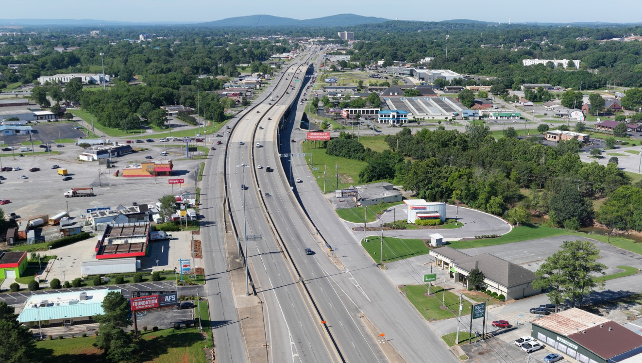 An aerial view of a highway with a four-lane mainline and service roads. The mainline includes an overpass at the junction with another highway.