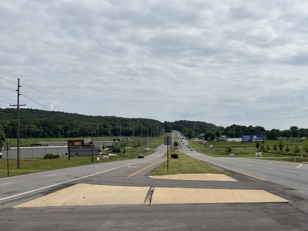 Traffic travels on a four-lane highway divided by concrete islands and grassy medians,