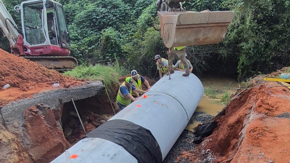 Construction crew guiding the installation of a large drainage pipe during a pipe replacement project on SR-605.