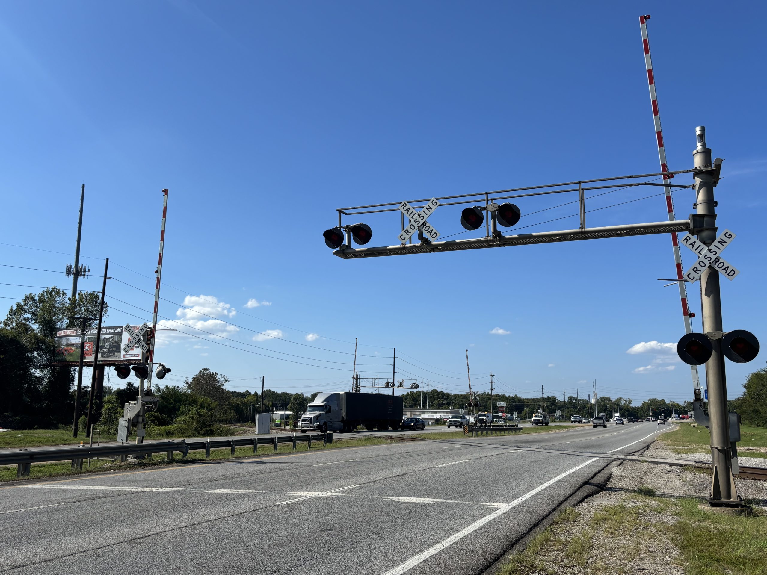 A railroad crossing with gates and signals on a divided six-lane highway.