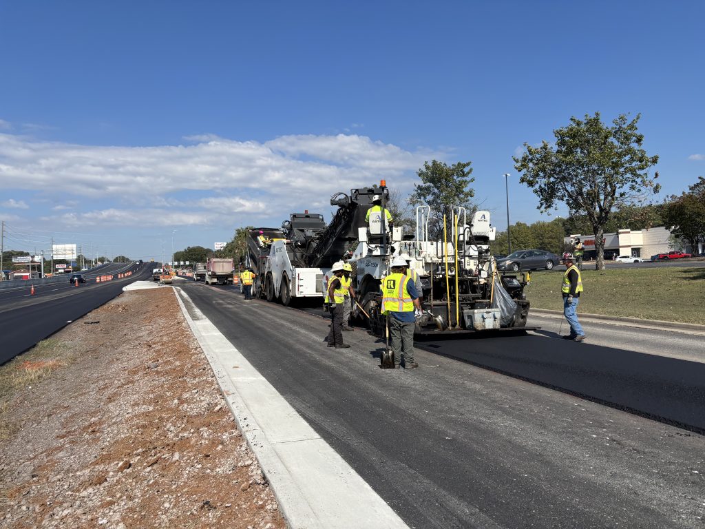 Workers follow equipment paving a road.
