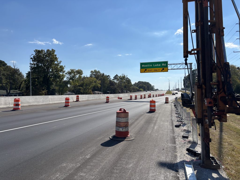 A new overhead sign for Mastin Lake Road over a new road lined with drums. A guardrail truck sits in the foreground.